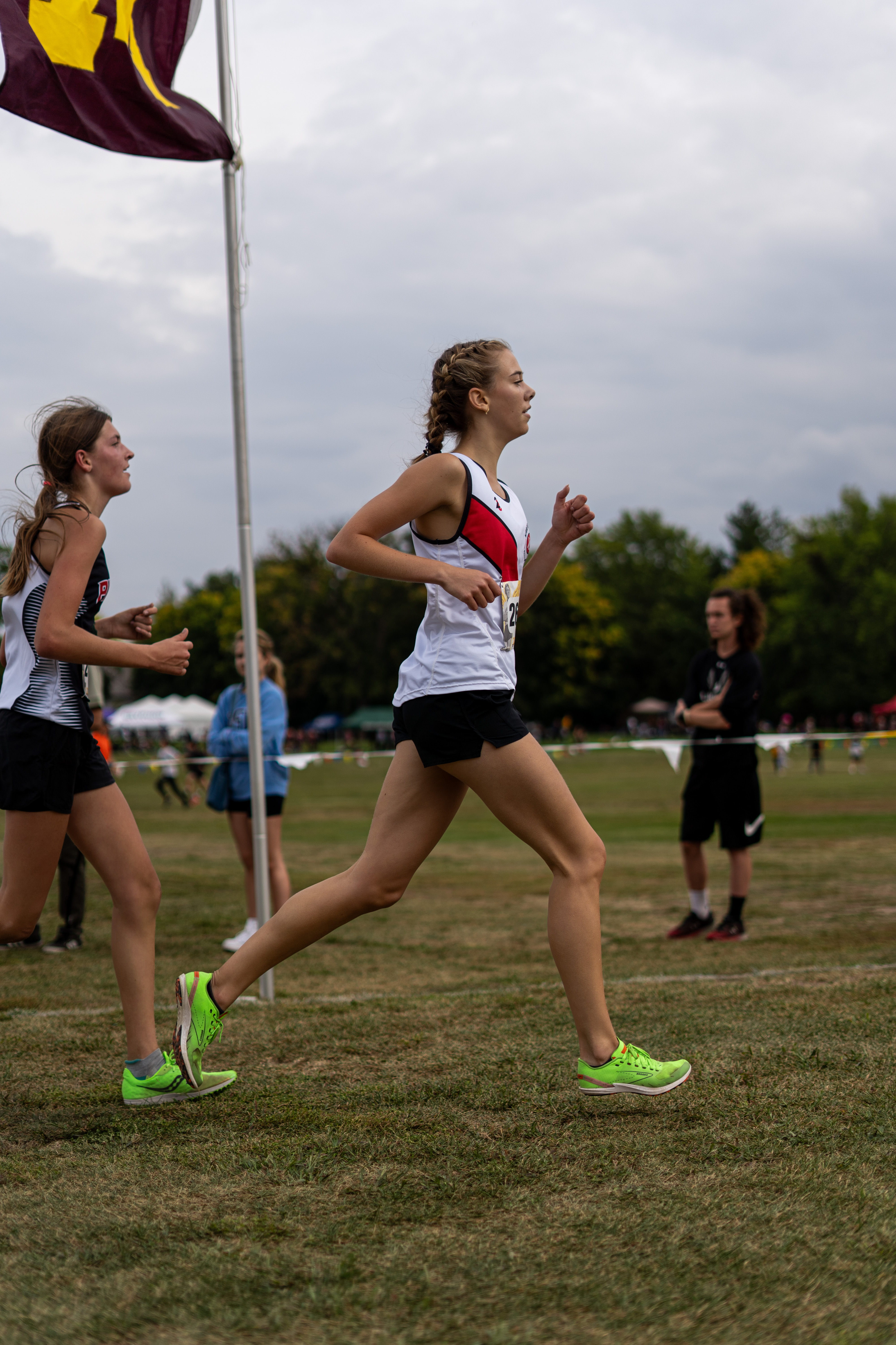 Two female runners race on a grassy field, one in the foreground with bright green shoes.