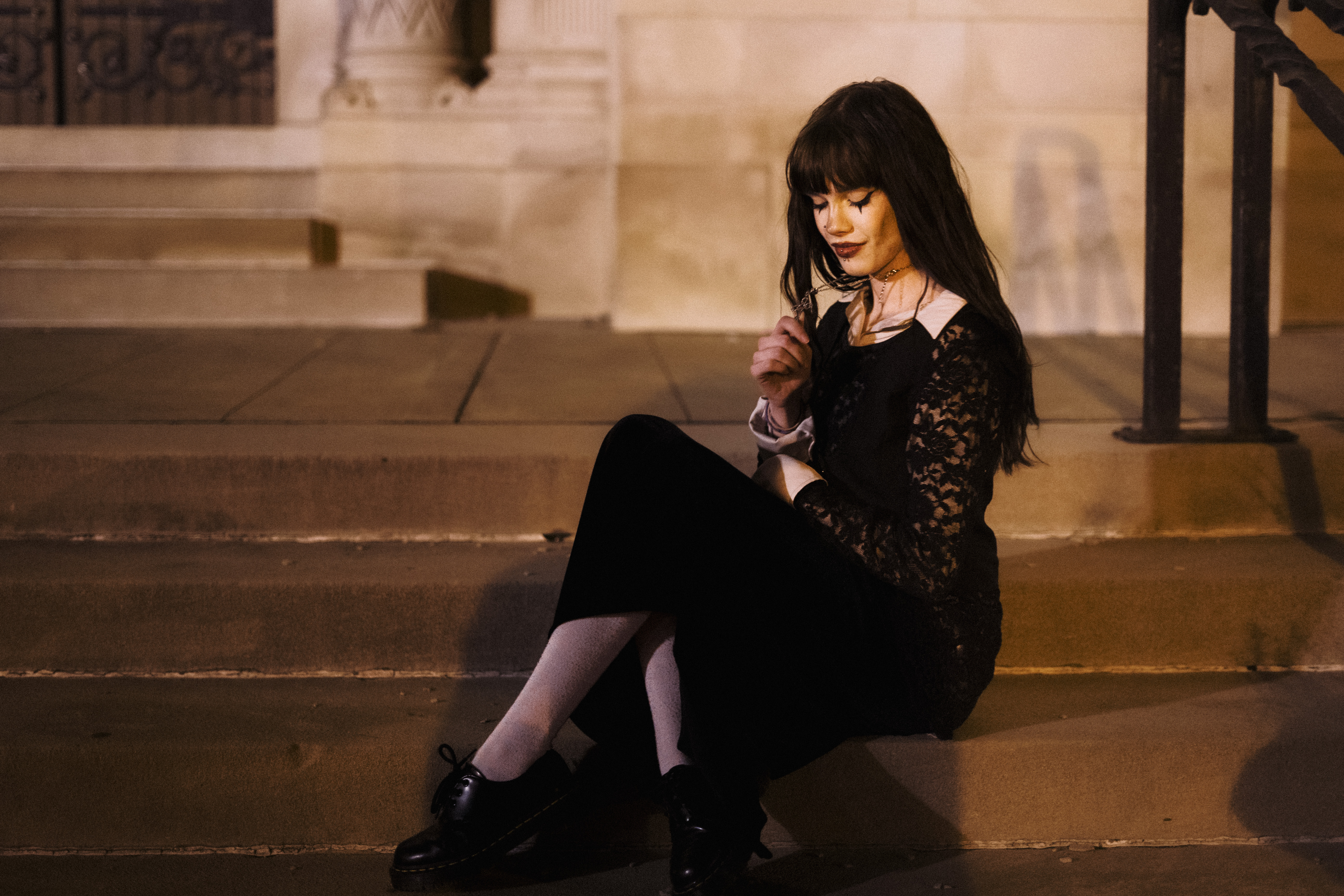Woman in black lace dress sitting on steps at night.
