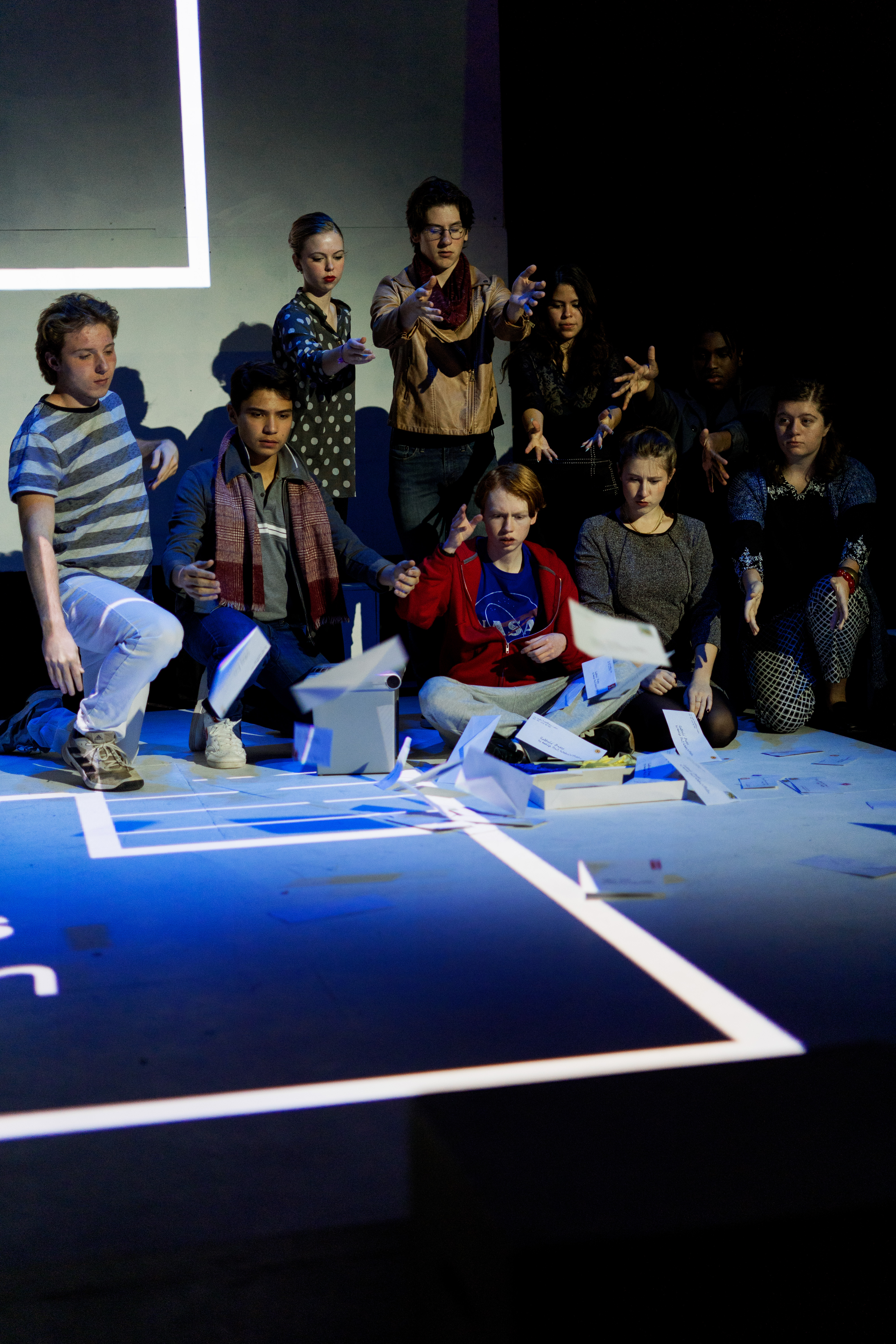 A group of young actors on a stage, throwing papers in the air during a performance.